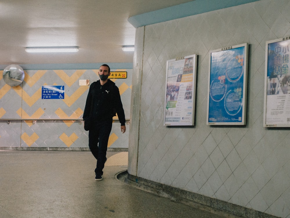 a man walking down a hallway next to posters