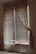 A dimly lit room with a window covered by wooden blinds and sheer lace curtains. The blinds are partially open, allowing some light to filter through, creating a gentle contrast of light and shadow on the walls and floor. The curtains drape elegantly on either side of the window, adding a vintage or rustic feel to the scene.