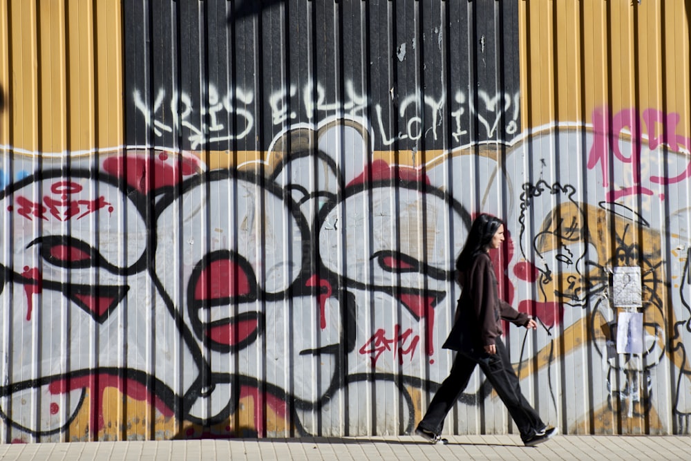Una persona caminando más allá de una pared con graffiti en ella