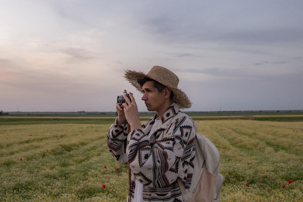 夢のようなおとぎ話の夕日の間に美しいカモミール畑の真ん中で写真を撮る若い男