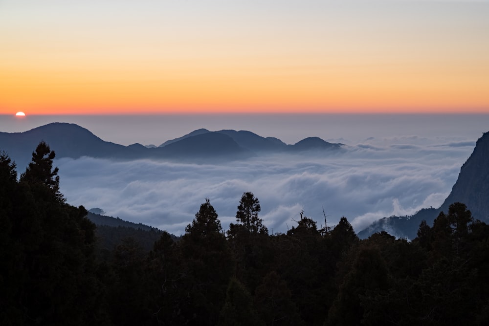 the sun is setting over the clouds in the mountains