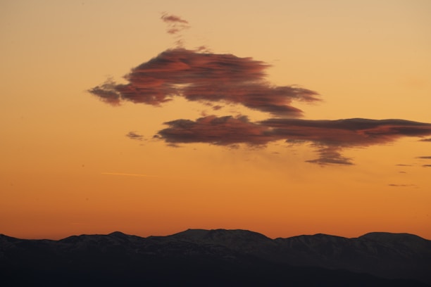 A striking photo of a dramatic storm cloud rolling over a serene landscape at sunset.