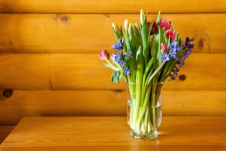 A sleek transparent glass vase filled with fresh spring flowers on a wooden table.