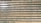 An array of long, parallel rows of solar panels is arranged on a barren, sandy landscape. The panels are aligned neatly, with sunlight reflecting off some of them, creating a shimmering effect. Sparse patches of green are visible between the rows, highlighting the arid environment.