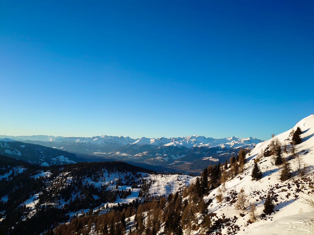 a view of a snowy mountain with trees and mountains in the background