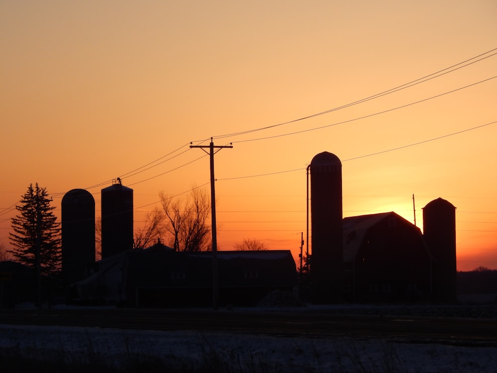 the sun is setting over a farm and silos