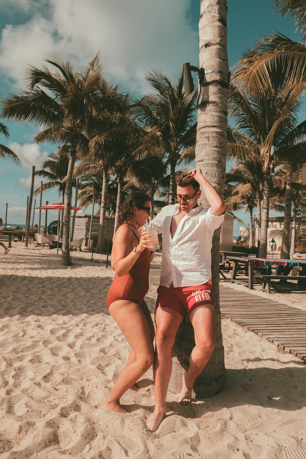 a man and a woman standing on a beach next to a palm tree