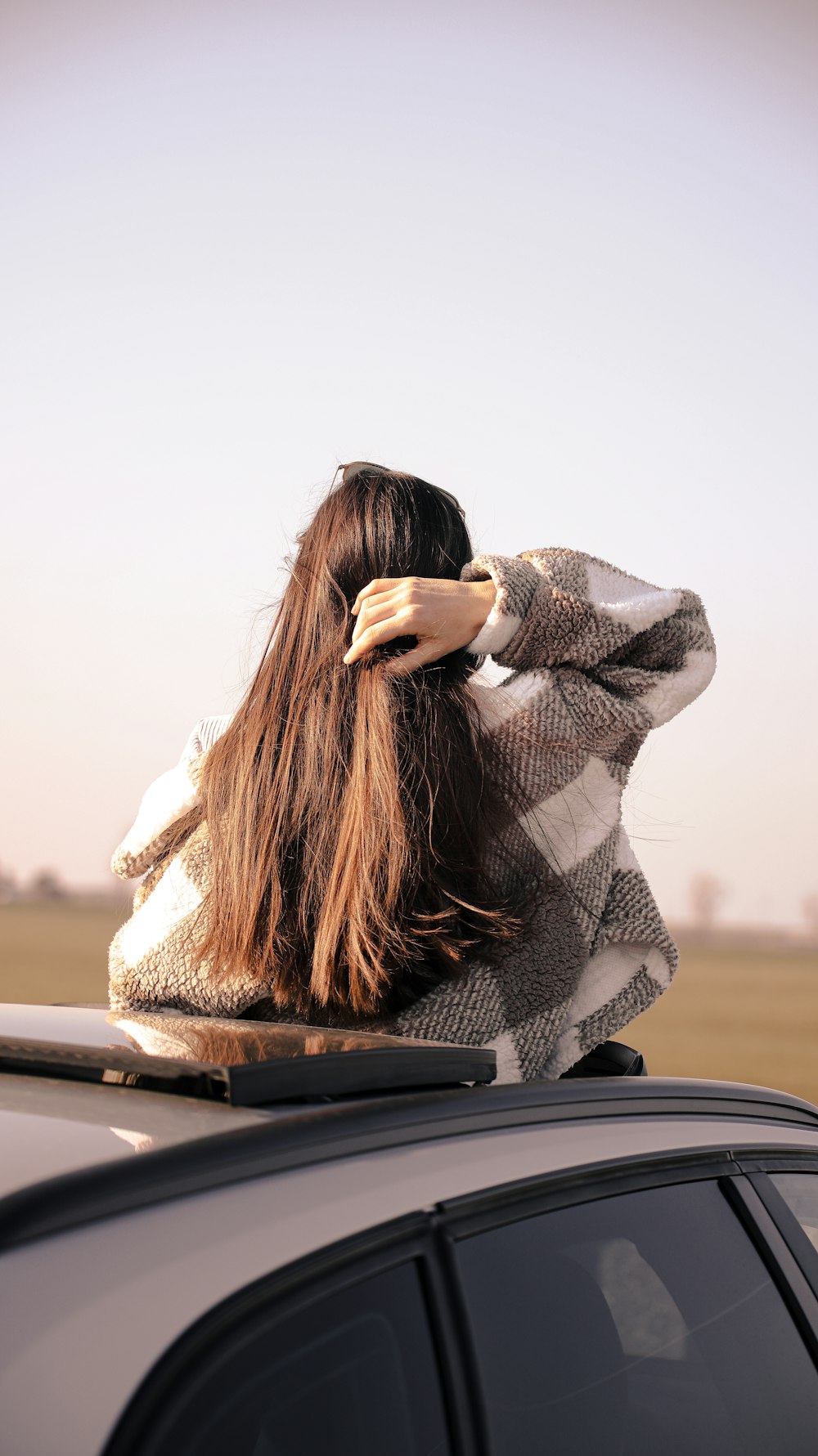 a woman with long hair sitting on top of a car
