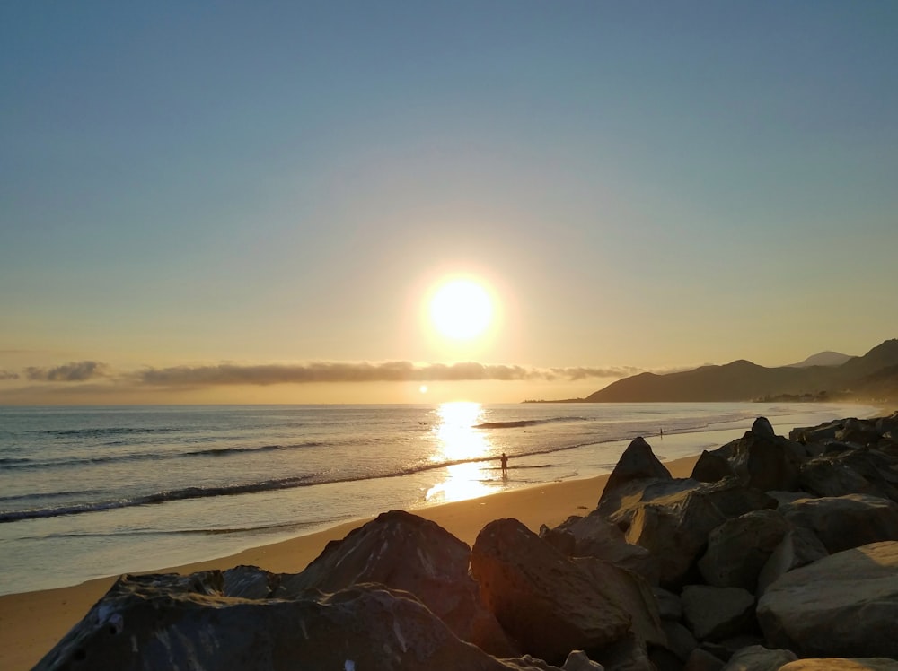 the sun is setting over a beach with rocks