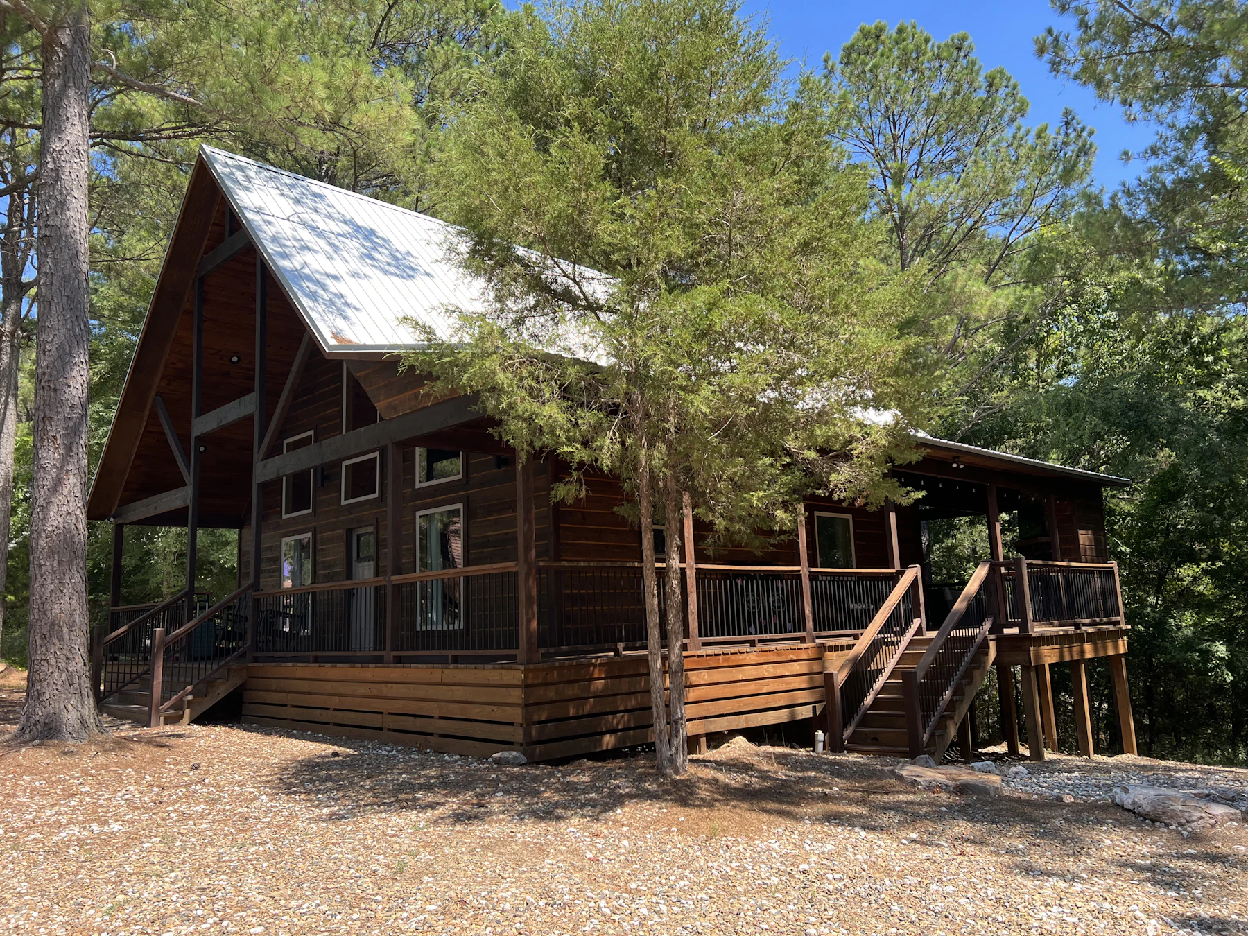 Mountain cabin with wraparound timber deck, wood stairs, and dark metal railing among pines