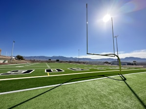 Wide view of a freshly installed synthetic turf football field under bright Monterrey sky.