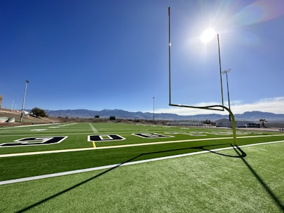 Wide view of a freshly installed synthetic turf football field under bright Monterrey sky.