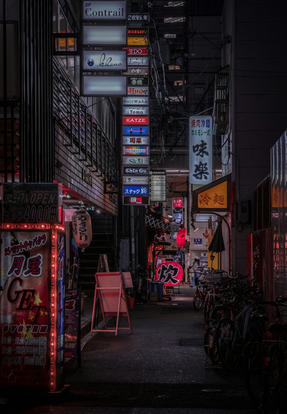 a dark alley with neon signs and chairs