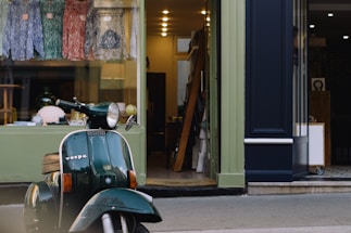 A friendly customer service representative smiling beside a Vespa scooter with branded merchandise in the background.
