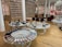 A chic showroom with stylish furniture and elegant displays of women's footwear, featuring flats, sandals, and boots. The wooden flooring and luxurious red chairs create a sophisticated ambiance, with a chandelier adding a touch of elegance. Shelves in the background appear to store stacked ballet shoes.