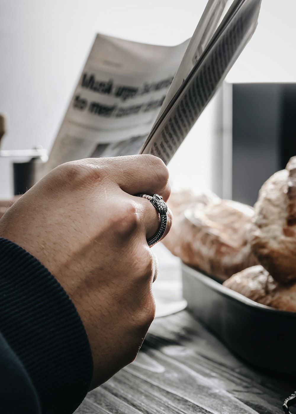 a person is reading a newspaper while holding a croissant