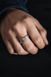 Close-up of the sleek mf ring glowing softly on a person's finger against a dark background.