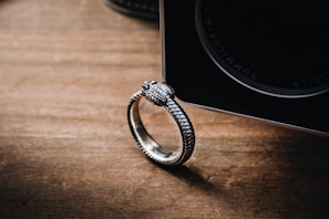 A close-up of a delicate silver ring on a wooden surface.