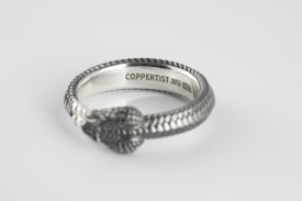 A silver ring designed to resemble a snake with intricate scale details. The inside of the band is engraved with text, including 'COPPERTIST.WU' and 'S925'. The image captures the ring on a plain white background, emphasizing the craftsmanship and texture of the metalwork.