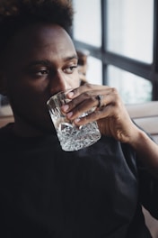 A person is sitting and holding a crystal glass close to their face, gazing thoughtfully out of the window. The light entering through the window casts soft shadows inside the room, creating an intimate and relaxed atmosphere.