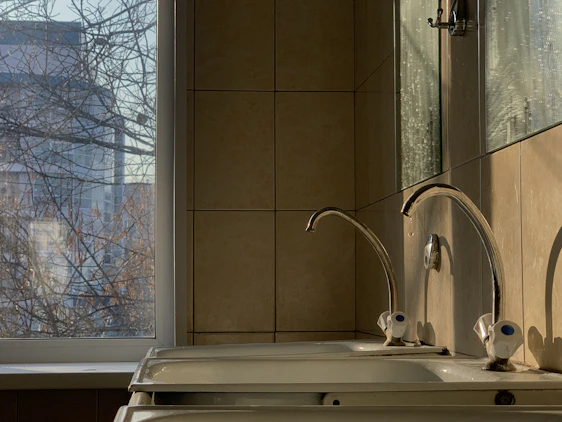 A confident plumber in blue uniform inspecting a home's kitchen sink in a sunlit Buckhead residence.