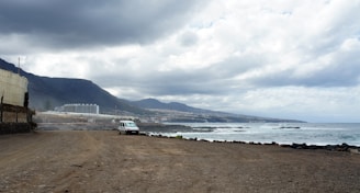 A compact car parked in front of a scenic coastal road in Biguaçu.