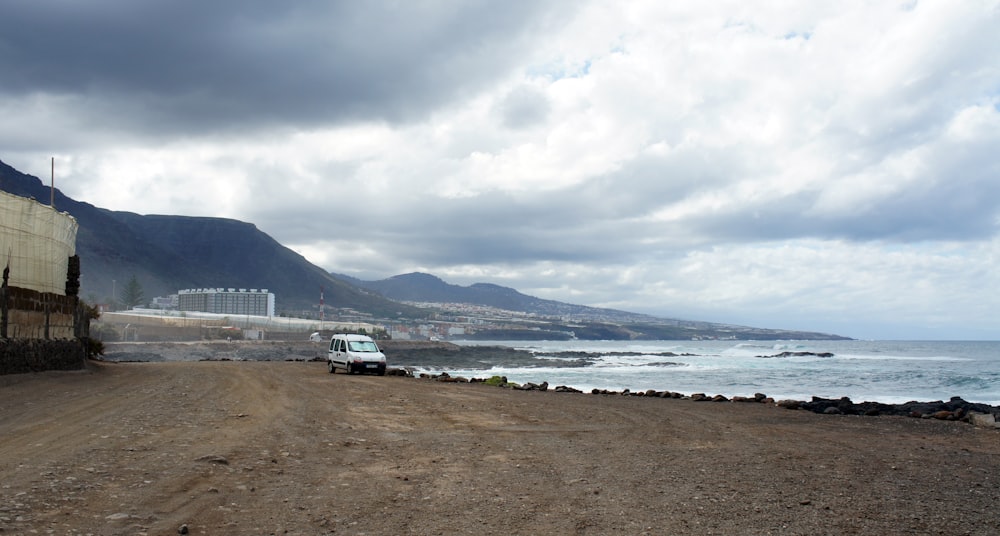 a truck driving down a dirt road next to the ocean