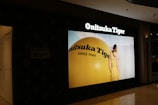 A store display showcases a large advertisement for Onitsuka Tiger, featuring a person in a yellow outfit standing next to a giant yellow sphere with the brand's name and 'Since 1949' written on it.