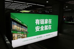 A large illuminated advertisement is displayed in an indoor setting, primarily showing a real estate company's branding. The sign features a green background with white text and includes an image of a building with the company's name, Lianjia, on it.