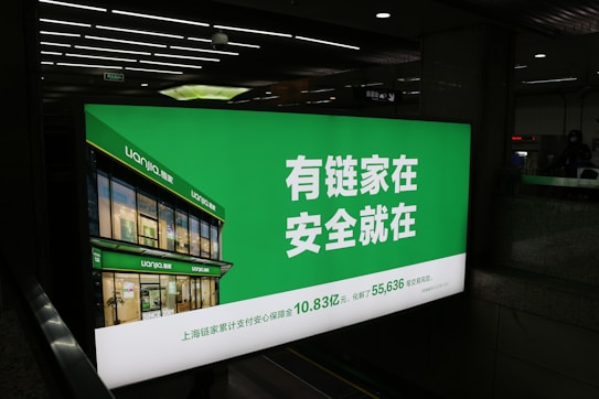A large illuminated advertisement is displayed in an indoor setting, primarily showing a real estate company's branding. The sign features a green background with white text and includes an image of a building with the company's name, Lianjia, on it.