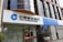 A modern bank building with a prominent sign in both Chinese and English for China Construction Bank. The facade features large, reflective windows and a clean, structured architectural design. Potted plants are placed near the entrance, giving it an inviting look.