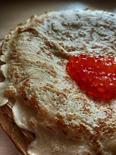 A stack of thin, golden-brown crepes with a dollop of vibrant orange-red caviar on top, creating a contrast in texture and color.