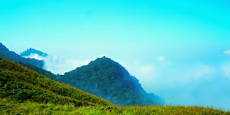 Lush green hills rolling under a bright blue sky, perfect for hiking adventures.