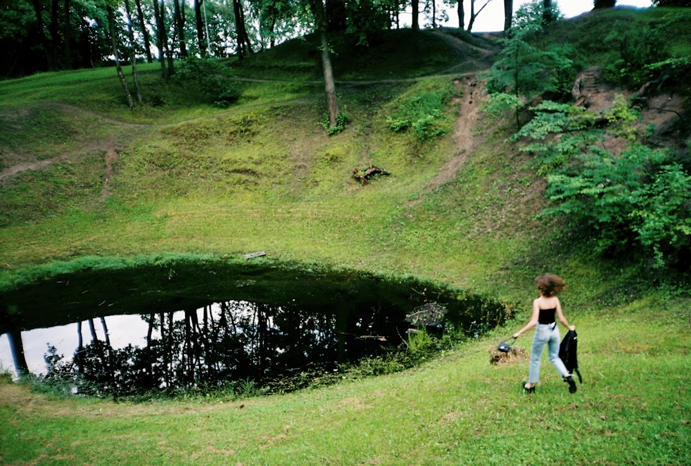 a woman walking a dog on a leash near a pond