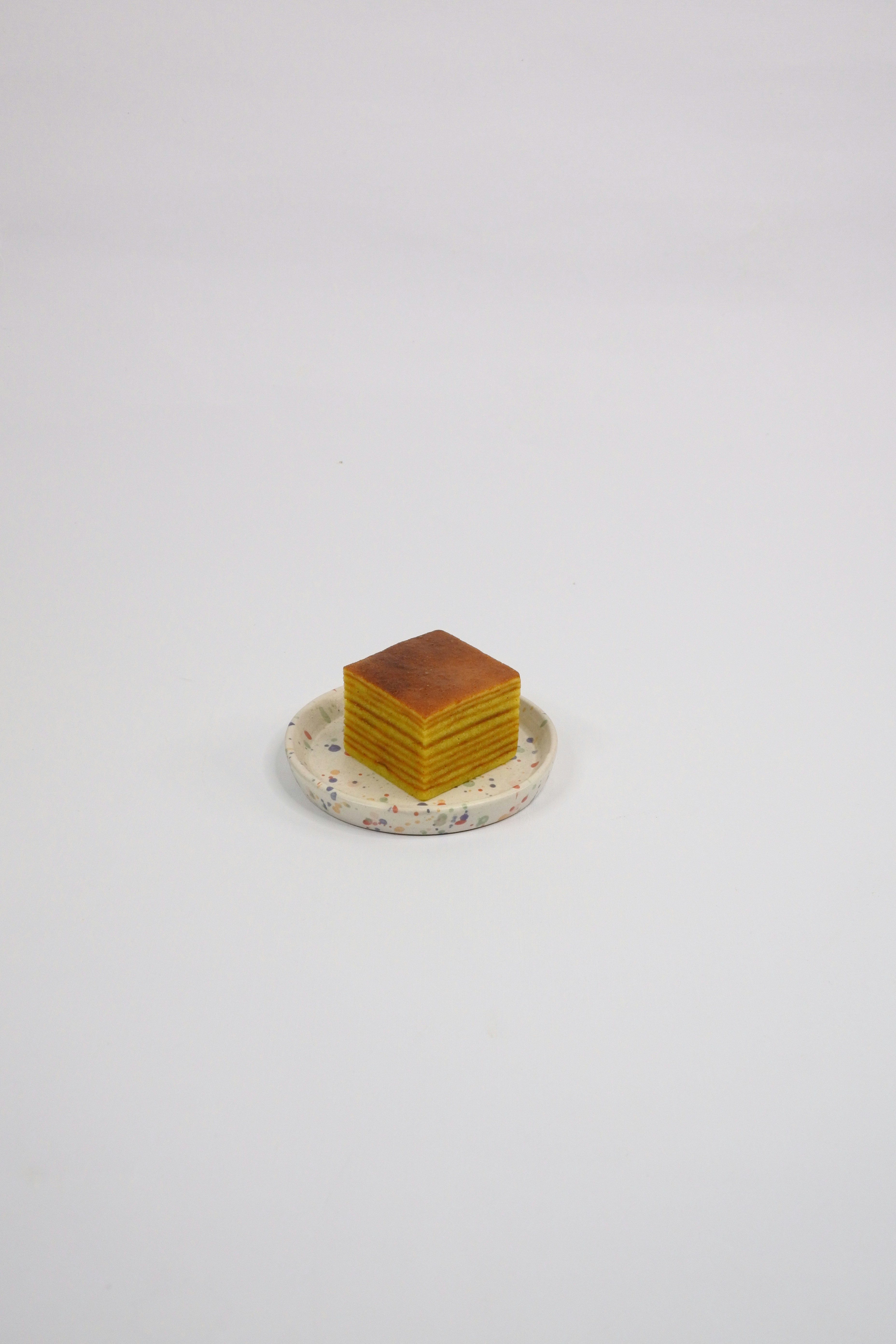 Soft yellow layered cake slice on dark ceramic plate, warm amber studio lighting, rich texture