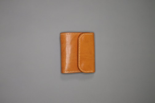 A tan leather wallet is placed on a plain gray surface. The wallet features white stitching along the edges and has a flap closure.