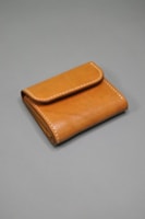 A brown leather wallet with visible stitching along the edges is placed on a plain gray surface. The wallet is neatly folded, showcasing its compact and minimalist design.
