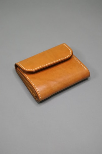 A brown leather wallet with visible stitching along the edges is placed on a plain gray surface. The wallet is neatly folded, showcasing its compact and minimalist design.