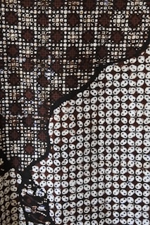 A complex pattern featuring circular and geometric motifs in a predominantly dark palette. The design includes interlocking circles and star-like shapes with a repetitive structure. The contrast between dark and light elements creates a visually striking effect.