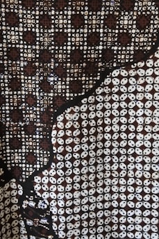 A complex pattern featuring circular and geometric motifs in a predominantly dark palette. The design includes interlocking circles and star-like shapes with a repetitive structure. The contrast between dark and light elements creates a visually striking effect.