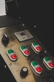 A control panel with various buttons featuring green and red sections, a black knob, and an LED display labeled 'Power Regulation'. The panel is metallic with engraved labels next to each control, including 'Power' and 'Drum'.