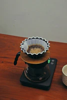 Minimalist setup of a French press and digital scale on a wooden table with natural light.