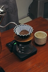 Kalita Wave brewer sitting on a wooden table with a gentle pour-over in progress.