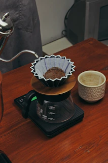 Photo of a pour-over coffee setup with a ceramic dripper and a glass carafe on a wooden table.