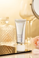 A sleek silver tube labeled 'Cosmetology Lady Cream' is prominently displayed. It stands upright on a reflective black surface, surrounded by elegant glassware and a soft pink rose, creating a luxurious and stylish setting.