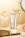 A sleek silver tube labeled 'Cosmetology Lady Cream' is prominently displayed. It stands upright on a reflective black surface, surrounded by elegant glassware and a soft pink rose, creating a luxurious and stylish setting.