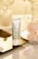 A tube labeled 'Cosmetology Lady Cream' is placed on a reflective surface. Surrounding it are decorative items such as a glass jar with a diamond pattern, a round mirror, and pink flower petals. The background features a soft, warm lighting that enhances the luxurious feel of the setting.