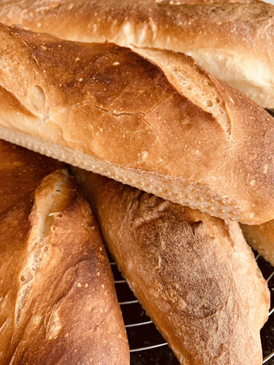 Freshly baked golden baguettes cooling on a rustic wooden shelf in a warm bakery.