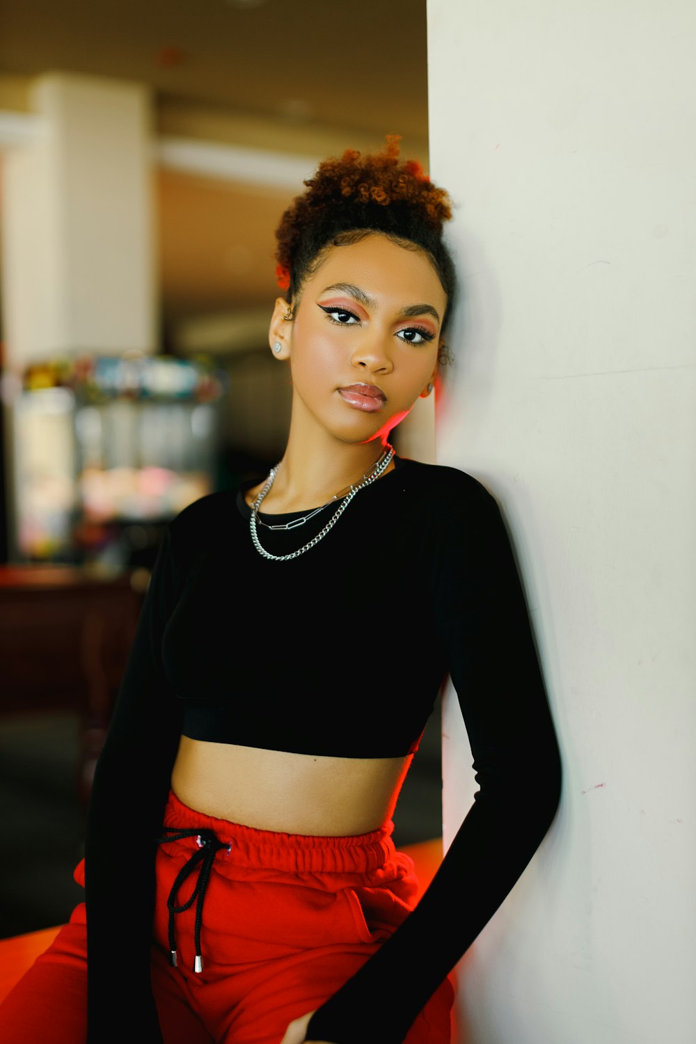 a woman leaning against a wall wearing a black top and red pants