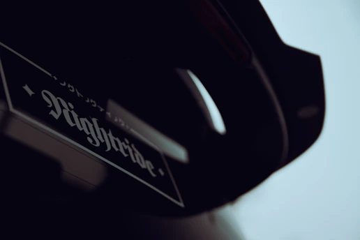A close-up of a vehicle with a sticker reading 'Nightride' with stylized fonts and possibly Japanese characters above it. The image is dark and the exact part of the vehicle is not clearly visible.